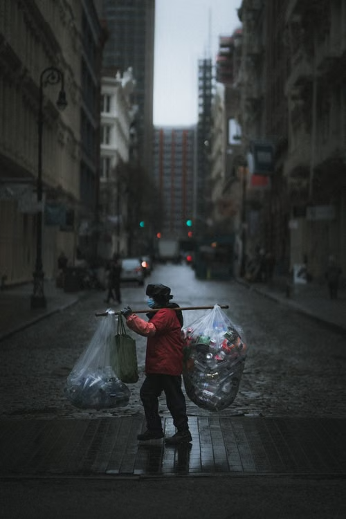 Waste collector carrying bags of sorted recyclables through a city street